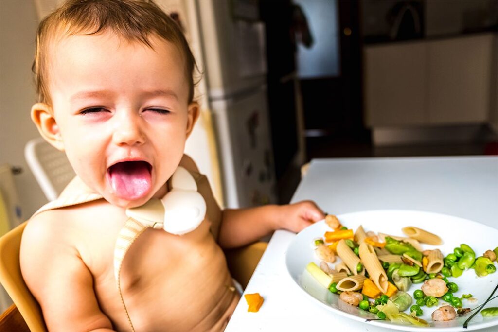 Bebé comiendo en la mesa con las manos y haciendo caras